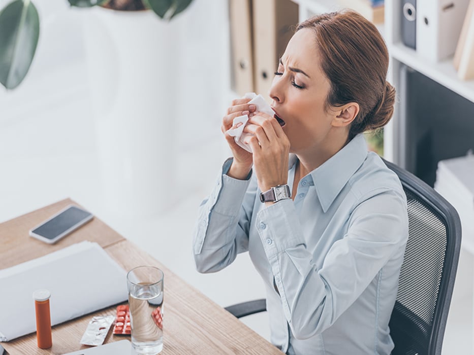 adult businesswoman sneezing at workplace