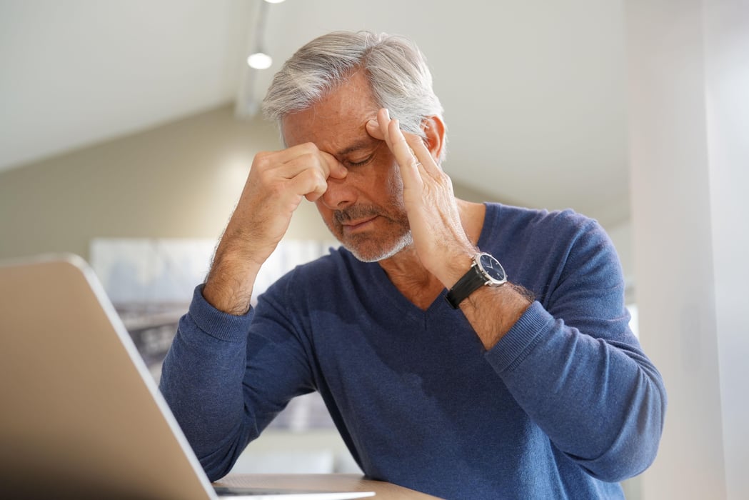Senior man having a headache while working on laptop computer long covid