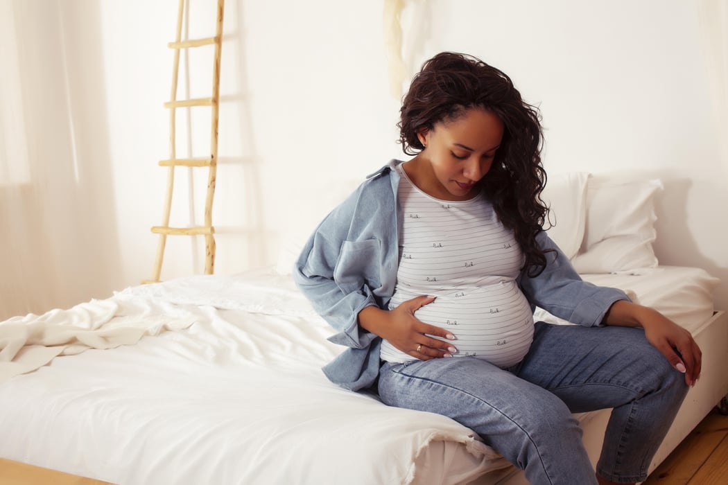 Black ethnic woman pregnant sitting on a bed