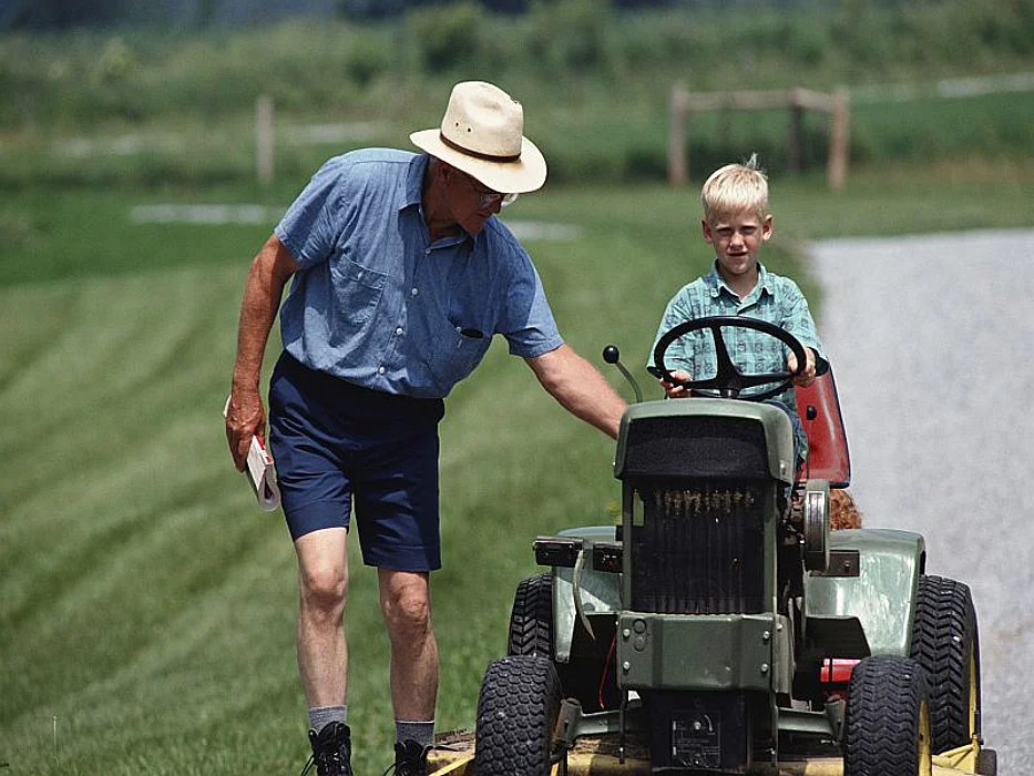 man teaching a boy to ride on a lawn mower