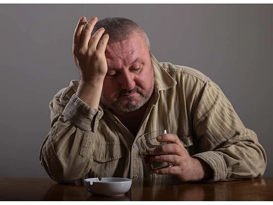 man smoking a cigarette looking on the glass with alcohol
