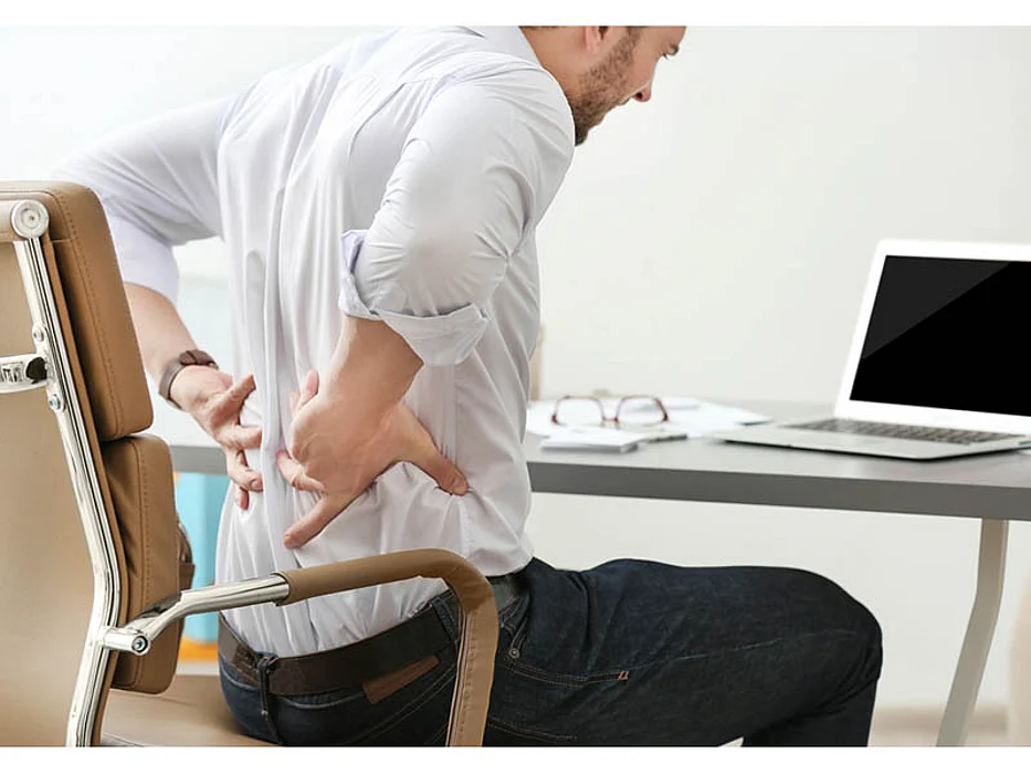 man holding his back in pain at the desk