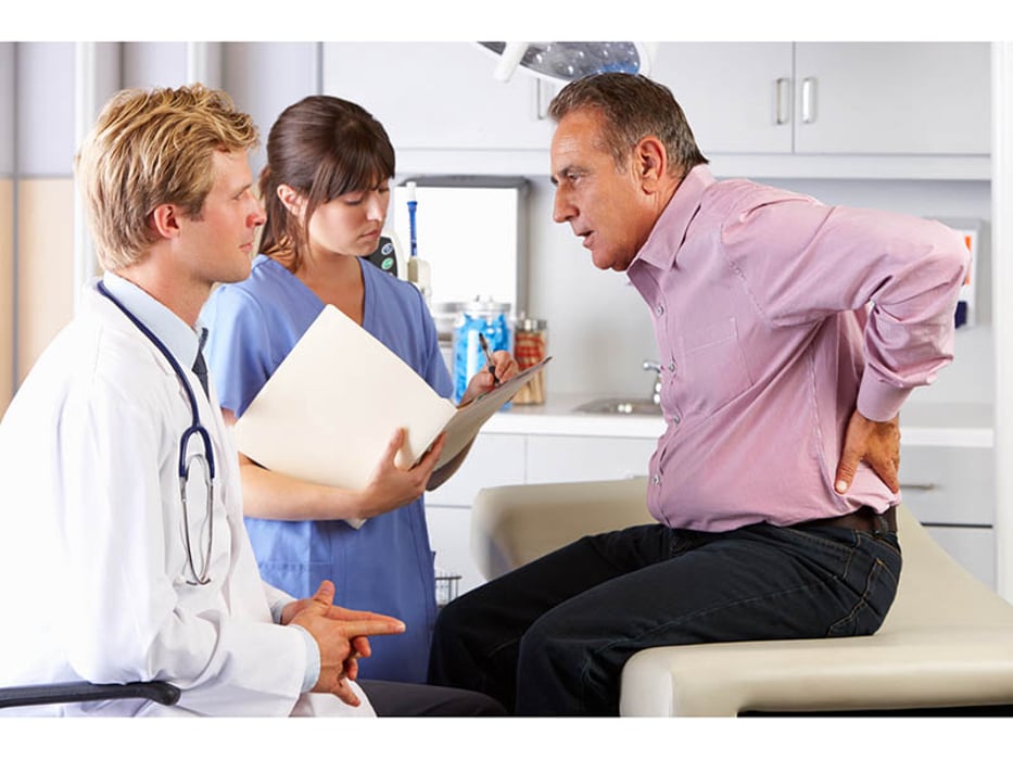 man holding his back in pain in front of two doctors