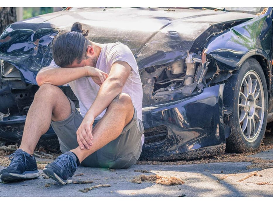 a man sitting on the ground in front of the crashed car
