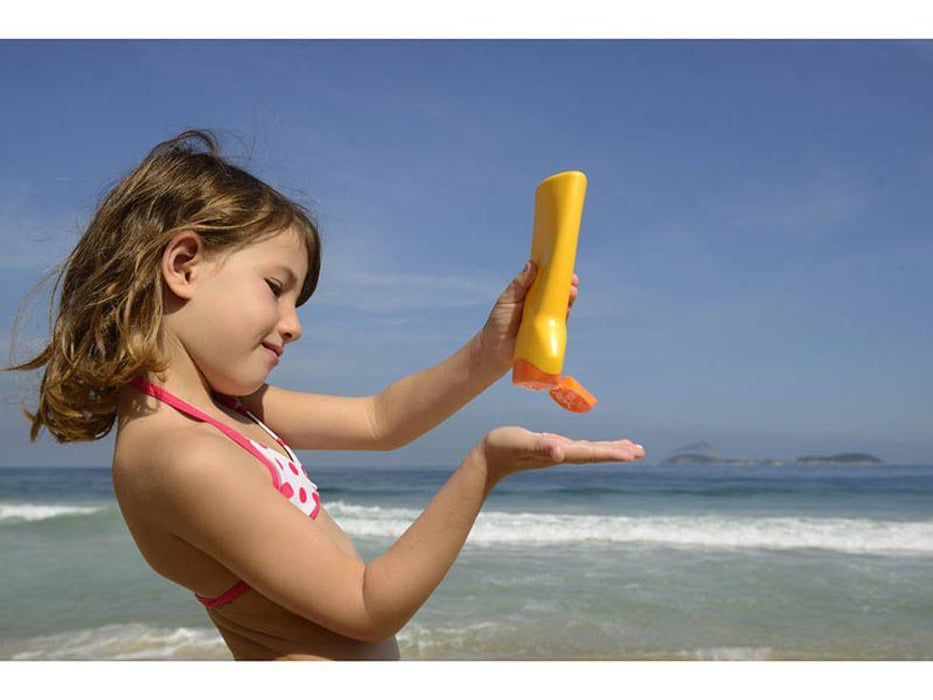 a little girl on the beach spreading sunblock on her skin