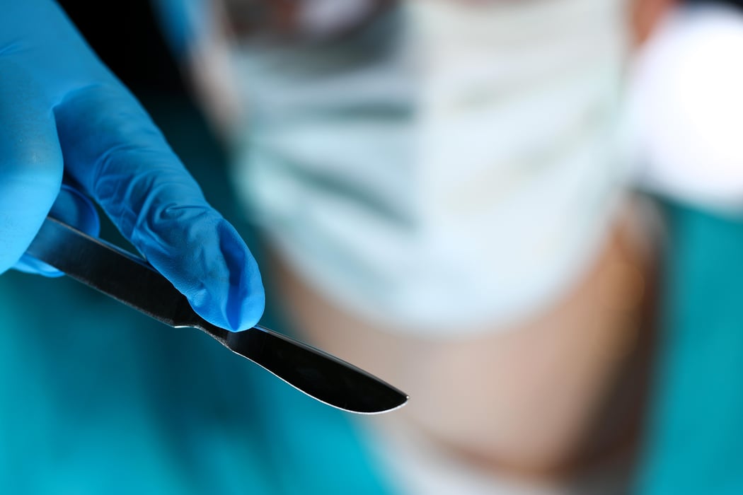 Surgeon arms in sterile uniform holding sharp knife