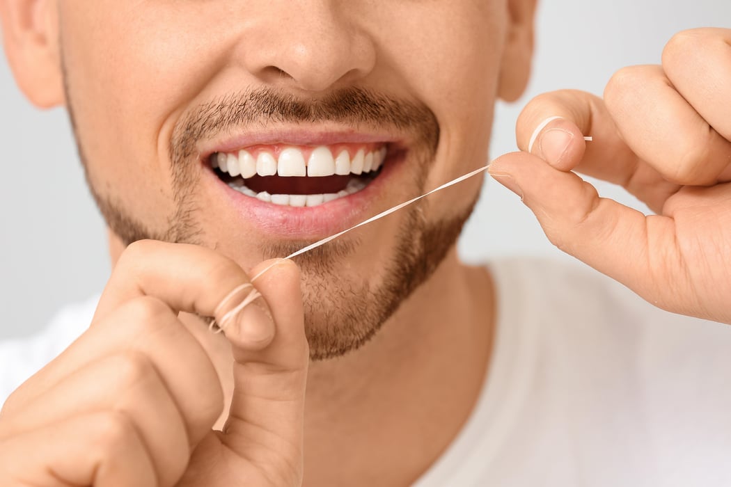 Handsome man flossing teeth on grey background, closeup