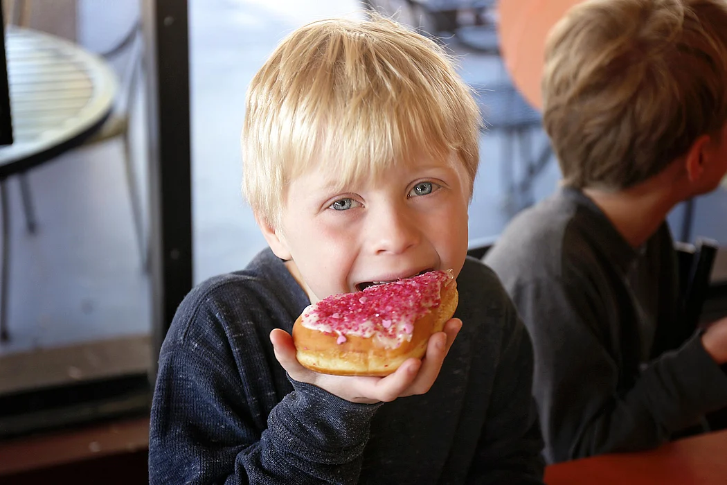 Little Boy Child Eating Forsted Donut at Bakery with his Family