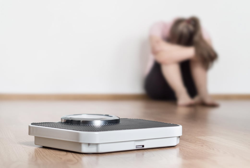 Dieting Weight loss fail concept. Scale and depressed, frustrated and sad woman sitting on floor holding head and arms on knees.