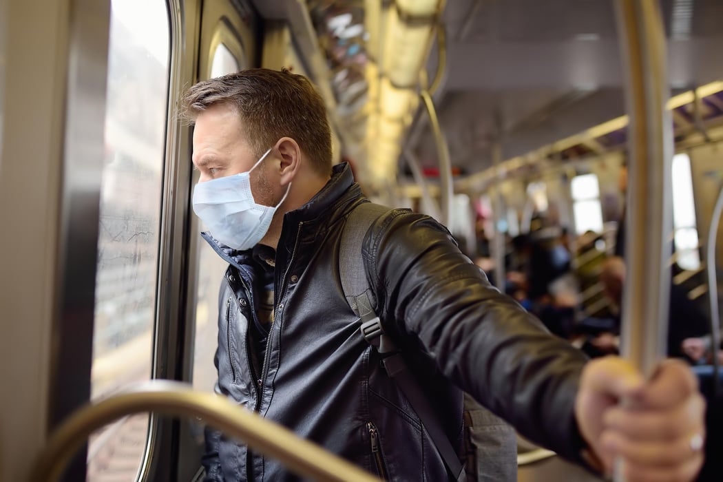 Mature man wearing disposable medical face mask in car of the subway during coronavirus outbreak.