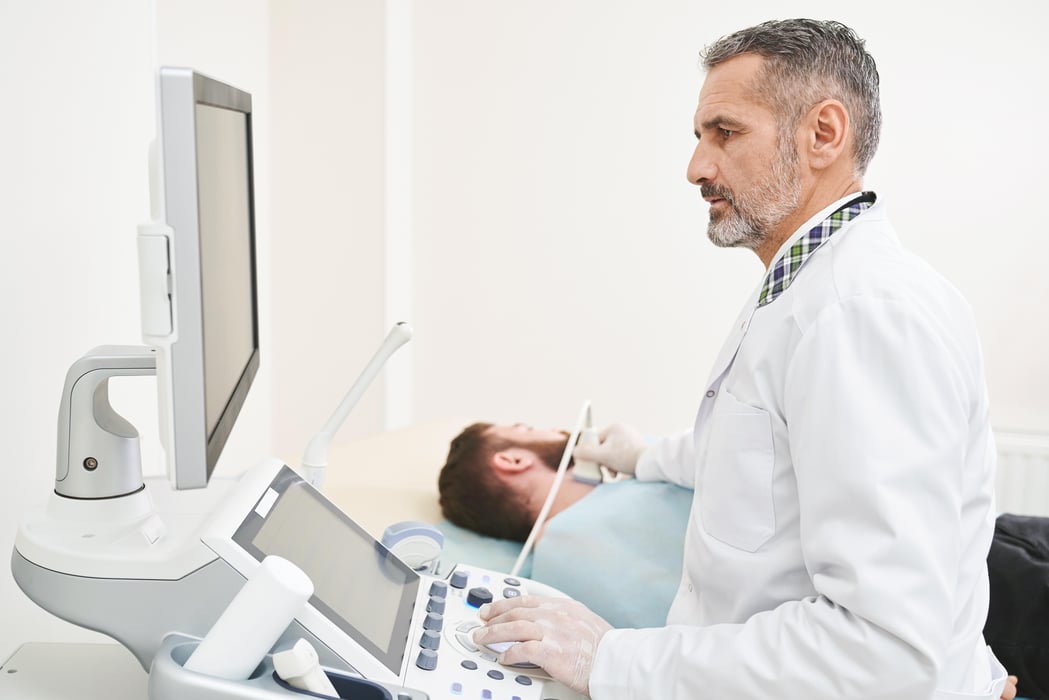Doctor sitting, looking at screen, doing diagnosis of neck.