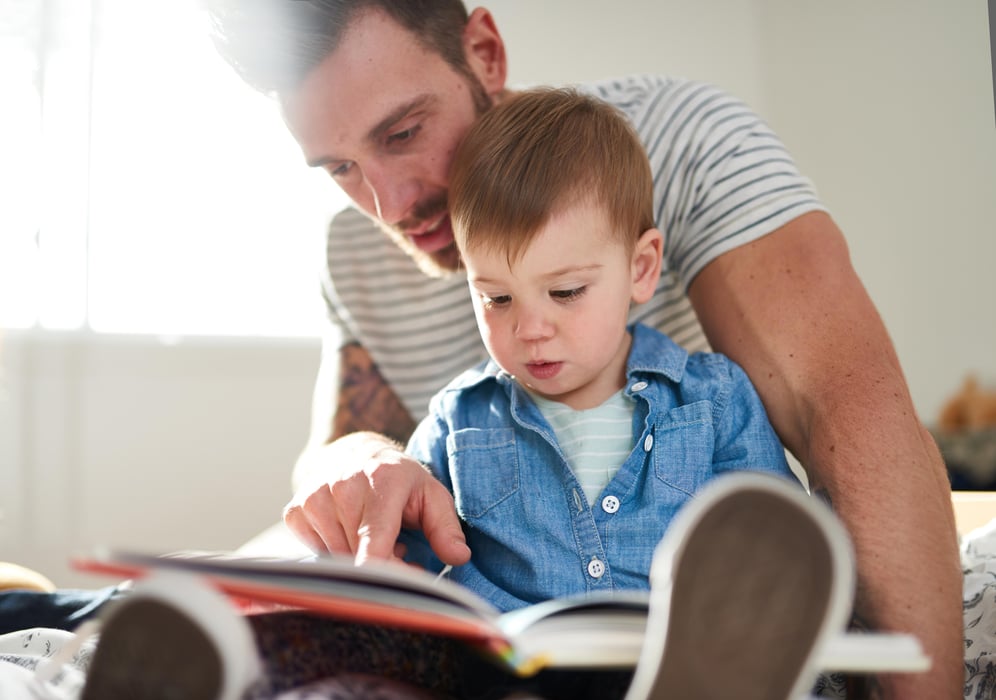  Female toddler learning to read book with father on bed