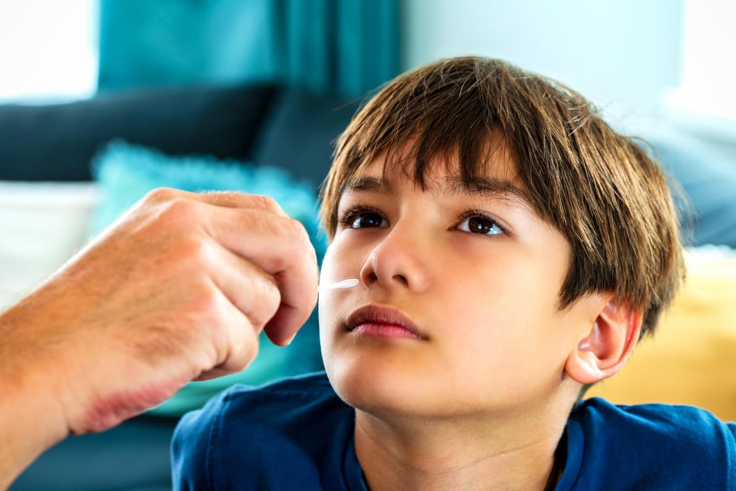 A parent do Covid-19 selftest at home for a son elementary age. A hand holding a cotton swab coronavirus antigen test kit into a child nose to use with SARS Cov 2 covid-19 rapid antigen test kits.