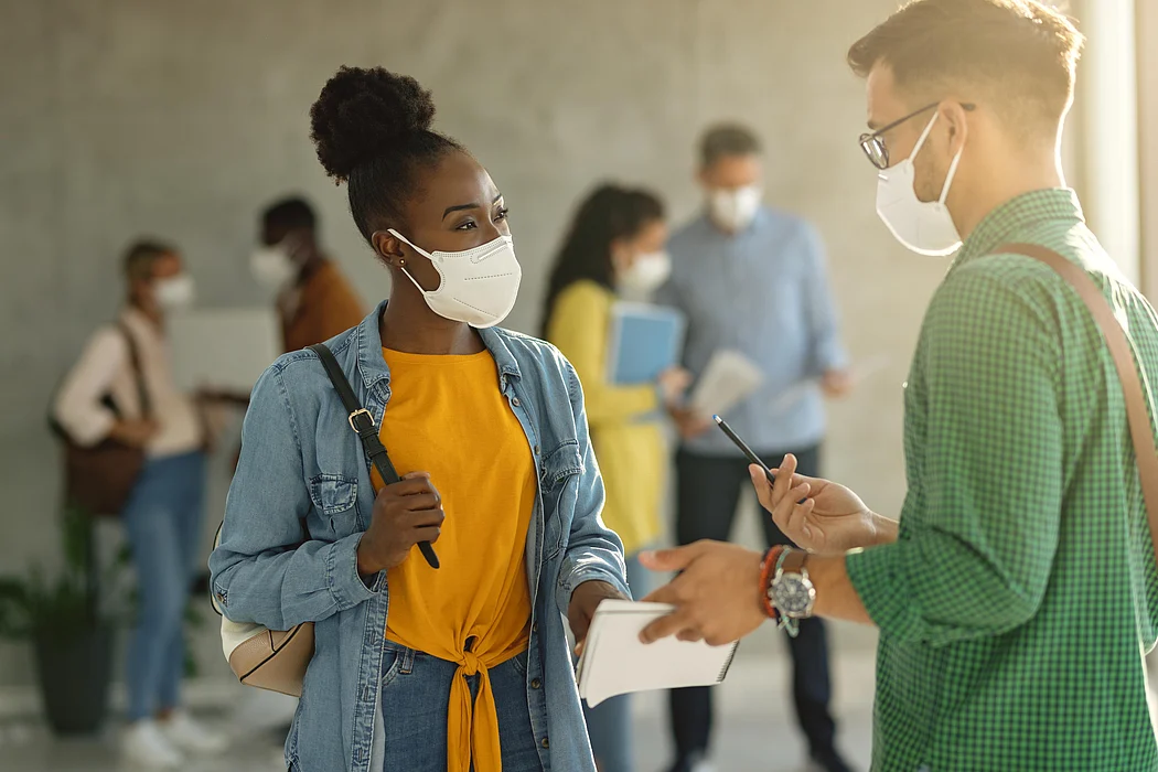 University students with protective face masks talking in a hallway.