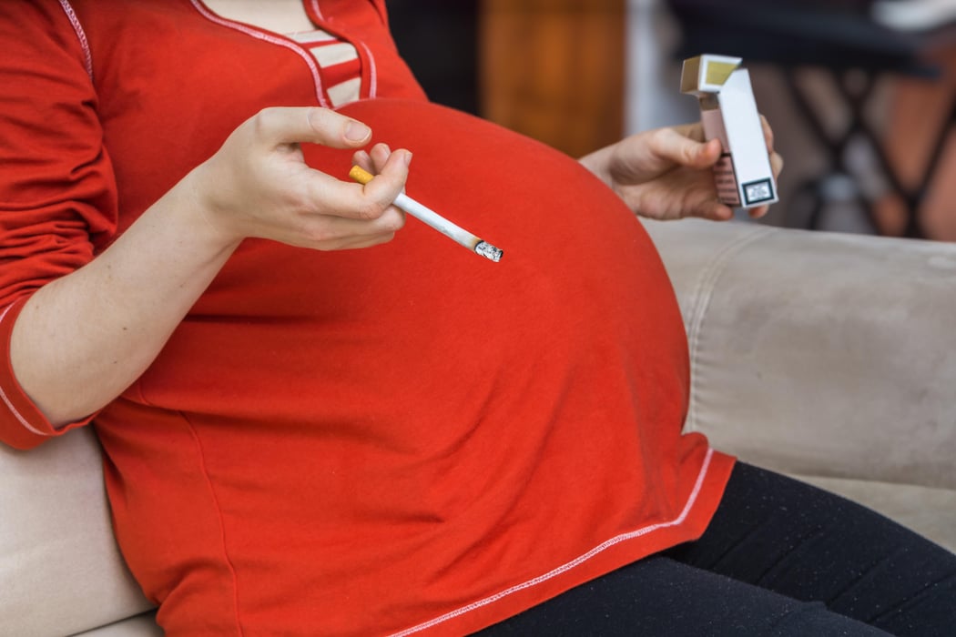 Pregnant mother holds cigarette in hand.
