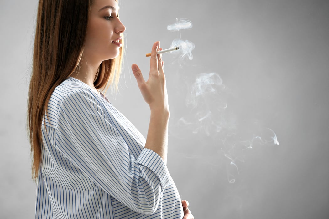 Pregnant woman smoking cigarette on grey background