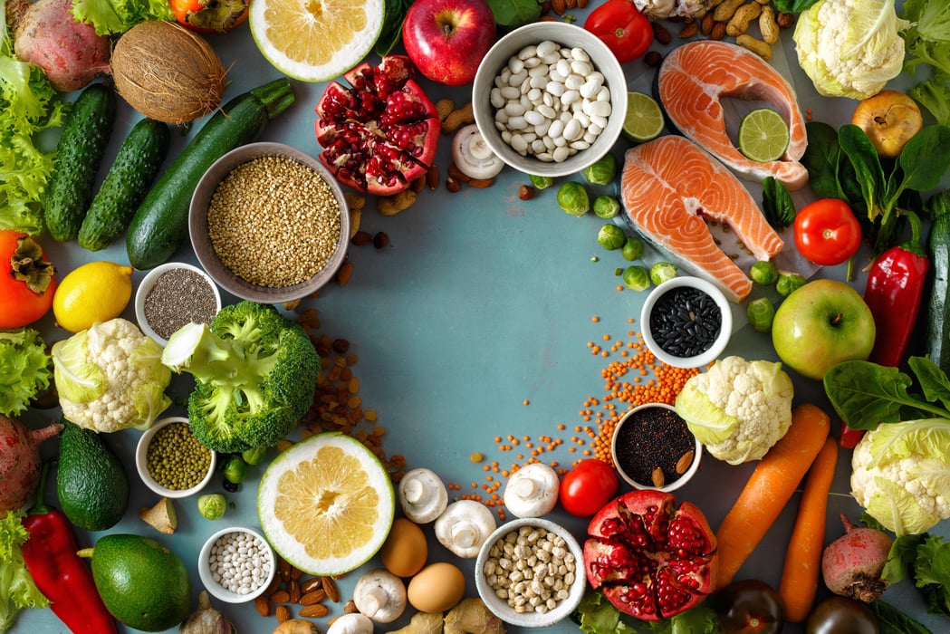 teal background with a variety of fruits , vegetables, legumes, whole grains, fish and spices laid out in a circle